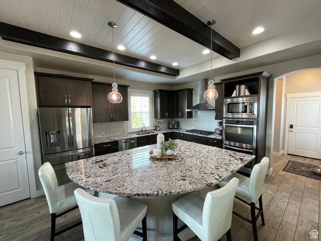 Chef kitchen featuring wall chimney range hood, stainless steel appliances, beamed ceiling, and an oversized quartz kitchen island | Image 11