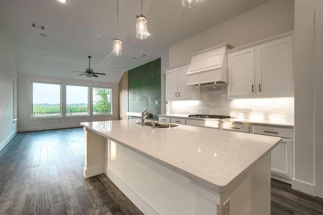 Kitchen with a sink, custom exhaust hood, stainless steel gas cooktop, dark wood-type flooring, and a kitchen island with sink | Image 7