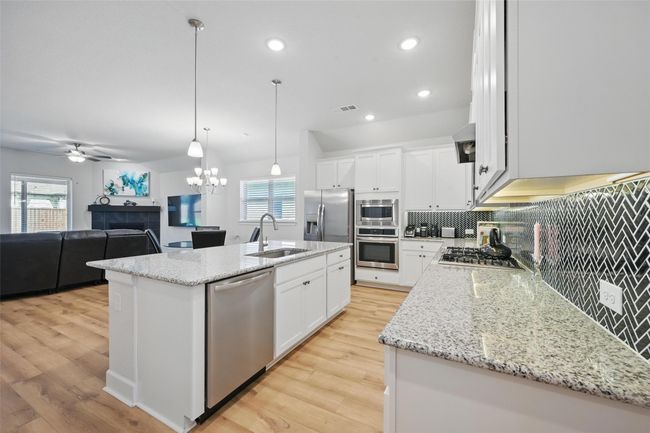 Kitchen featuring appliances with stainless steel finishes, a sink, backsplash, light wood-type flooring, and ceiling fan | Image 4