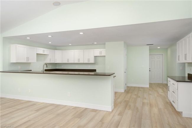 Kitchen with dark countertops, light wood finished floors, and white cabinetry. | Image 5