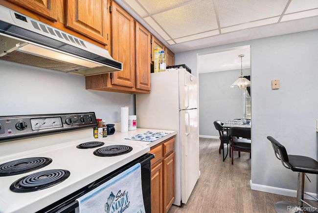 Kitchen with white appliances, brown cabinets, light countertops, under cabinet range hood, and a paneled ceiling | Image 10