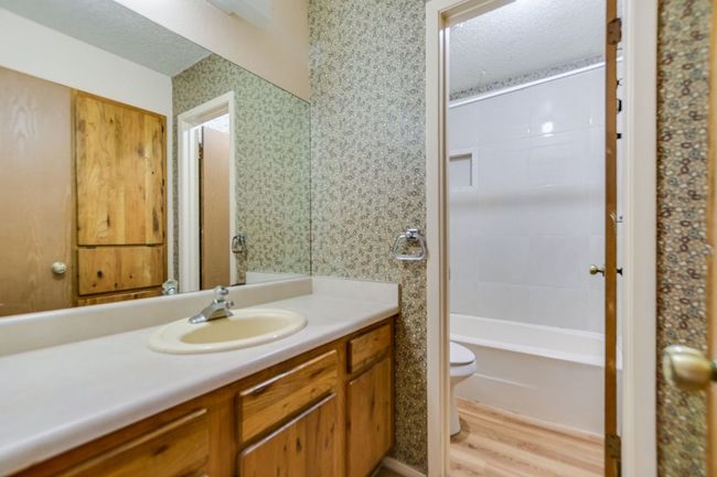 Bathroom with toilet, vanity, wood finished floors, a textured ceiling, and wallpapered walls | Image 16