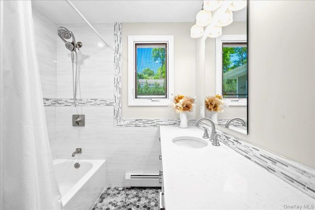 Bathroom with baseboard heating, vanity, tile walls, shower / tub combo, and a chandelier | Image 22