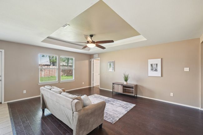 Living room featuring baseboards, a raised ceiling, visible vents, ceiling fan, and wood finished floors | Image 7