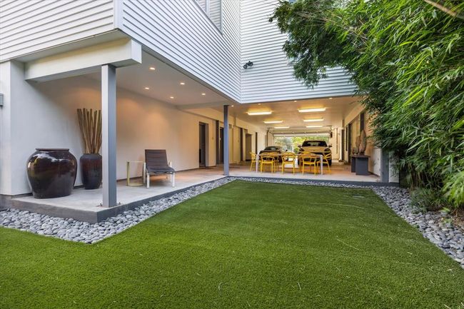 Versatile covered outdoor space blends function and style—perfect for entertaining, relaxing, or creative use. Seamlessly connected to the oversized garage, this area features sleek recessed lighting, modern architectural lines, and professionally landscaped touches, including synthetic turf and decorative river rock borders. Private and peaceful, with a natural bamboo screen providing added greenery and seclusion. A rare indoor-outdoor extension of livable space. | Image 39