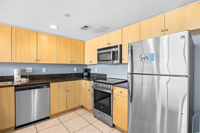 Kitchen with dark stone countertops, light brown cabinetry, visible vents, appliances with stainless steel finishes, and light tile patterned flooring | Image 4