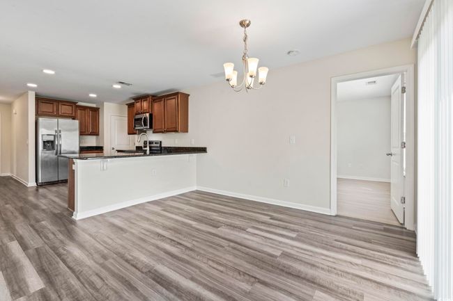 Kitchen with dark countertops, appliances with stainless steel finishes, a peninsula, a chandelier, and wood finished floors | Image 11