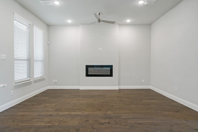 Unfurnished living room with recessed lighting, dark wood finished floors, a wealth of natural light, a ceiling fan, and a glass covered fireplace | Image 8