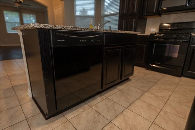 Kitchen with black appliances, light tile patterned flooring, decorative backsplash, and dark cabinetry | Image 32