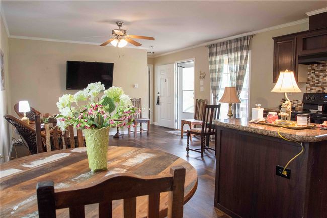 Dining area with dark wood-type flooring, ceiling fan, and ornamental molding open to living room and kitchen area | Image 24