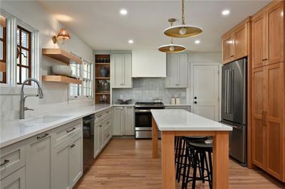 Kitchen with a kitchen island, hanging light fixtures, sink, appliances with stainless steel finishes, and light hardwood / wood-style floors | Image 1