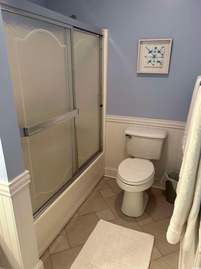 Full bath featuring a wainscoted wall, bath / shower combo with glass door, and tile patterned floors | Image 17