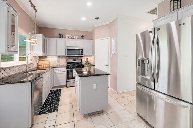 Kitchen with tasteful backsplash, a sink, appliances with stainless steel finishes, crown molding, and a kitchen island | Image 9