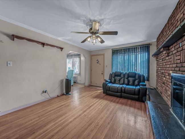 Living room with arched walkways, light wood-style floors, a ceiling fan, a brick fireplace, and crown molding | Image 4