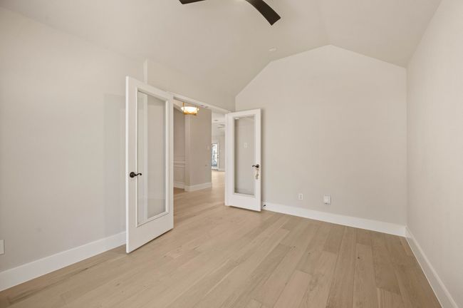 Empty room featuring french doors, light wood-type flooring, lofted ceiling, baseboards, and ceiling fan with notable chandelier | Image 6