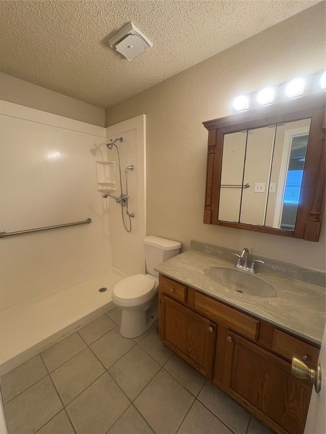 Full bath with a textured ceiling, toilet, tile patterned floors, vanity, and a stall shower | Image 12