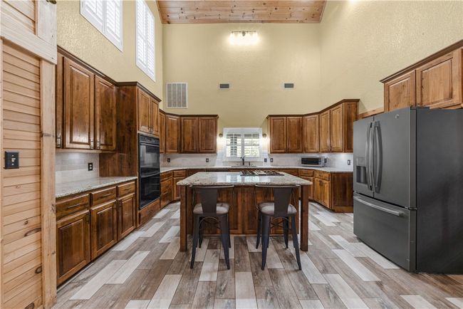 Kitchen with fridge with ice dispenser, a high ceiling, wood ceiling, a kitchen island, and a breakfast bar area | Image 11
