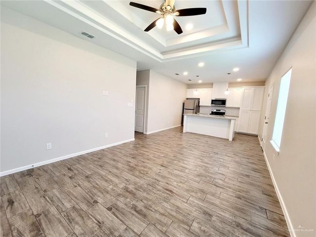 Unfurnished living room with ceiling fan, light wood-style flooring, recessed lighting, a tray ceiling, and baseboards | Image 12