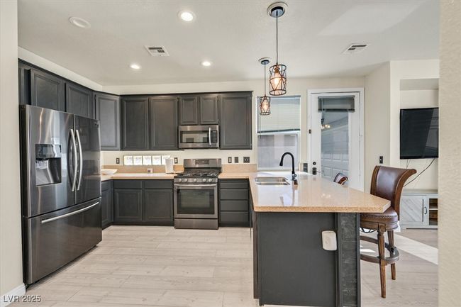 Kitchen with visible vents, a peninsula, light wood-style floors, stainless steel appliances, and a sink | Image 4
