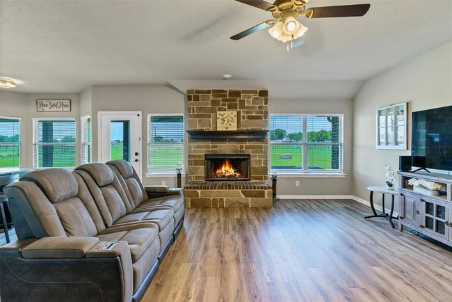 Living room with ceiling fan, vaulted ceiling, a fireplace, and wood-type flooring | Image 9