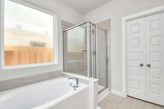 Experience a spa-like escape right in the heart of your primary bathroom. The expansive walk-in shower, surrounded by tile, and the distinctive garden tub with unique accents elevate your daily routine. The sophisticated vanity, featuring double sinks, dark-colored countertops, contemporary hardware, and bright recessed lighting, adds both style and functionality to the space. | Image 25