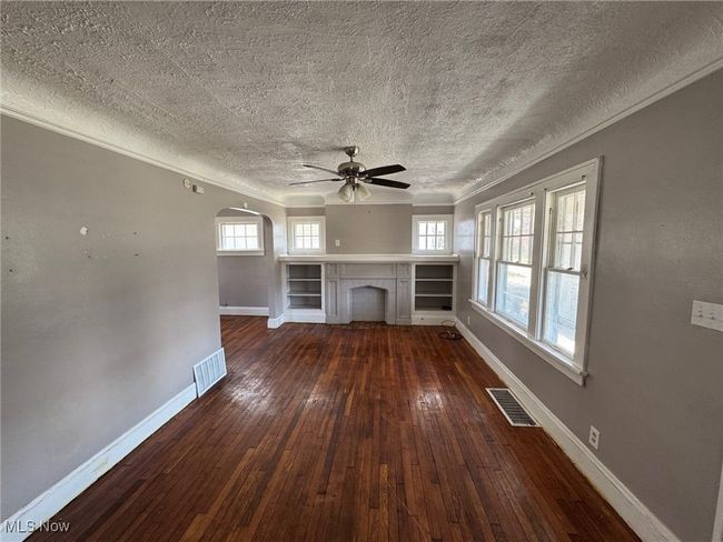Unfurnished living room with a textured ceiling, visible vents, baseboards, ornamental molding, and dark wood-style floors | Image 5
