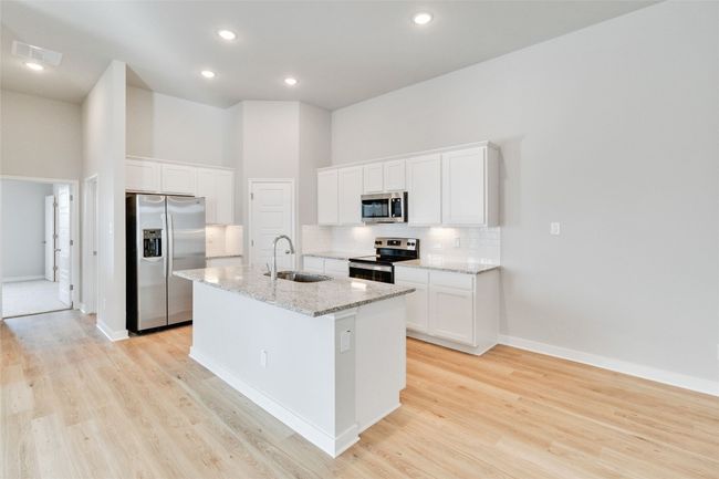 Kitchen with stainless steel appliances, backsplash, light wood-style flooring, a sink, and an island with sink | Image 13