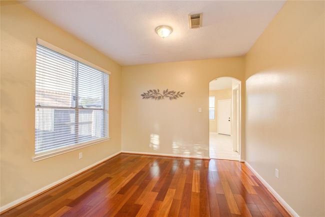 This room features warm wood flooring, neutral walls, and ample natural light from a large window. An arched doorway leads to another bright space, adding charm and openness. | Image 10