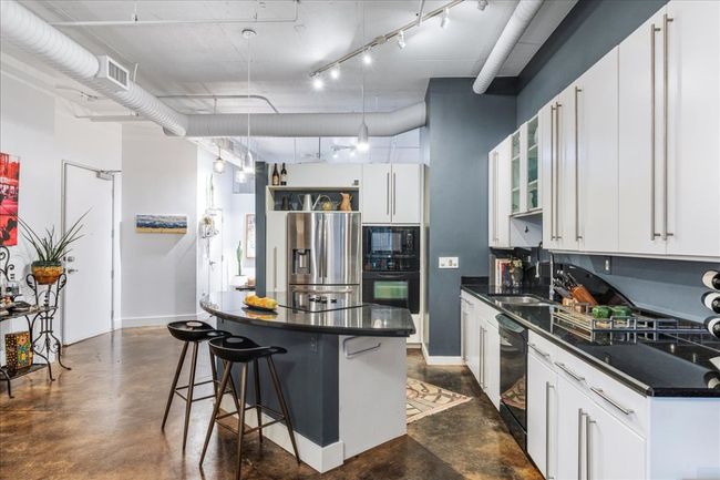 Kitchen featuring black appliances, dark countertops, concrete flooring, and a kitchen breakfast bar | Image 4