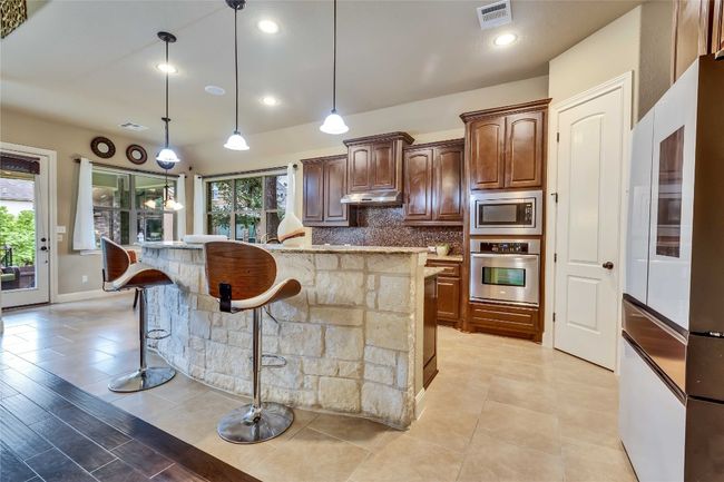 Gourmet kitchen featuring stainless steel appliances, under cabinet range hood, healthy amount of natural light, a breakfast bar, and recessed lighting | Image 24