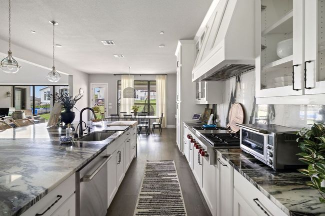 Kitchen featuring custom exhaust hood, glass insert cabinets, visible vents, stainless steel appliances, and a sink | Image 8
