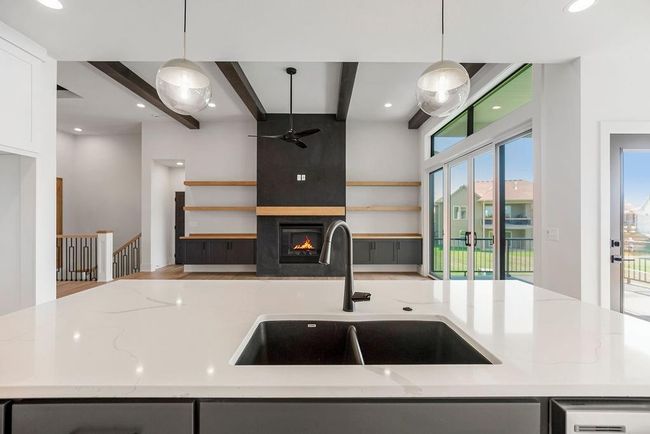 Kitchen with a sink, a ceiling fan, beamed ceiling, light stone counters, and decorative light fixtures | Image 9