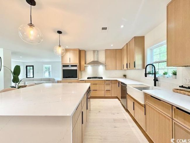 Kitchen featuring wall chimney exhaust hood, stainless steel appliances, light brown cabinets, light wood-style floors, and hanging light fixtures | Image 13