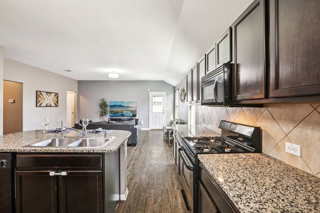 Kitchen with black appliances, dark wood finished floors, decorative backsplash, dark brown cabinets, and lofted ceiling | Image 6