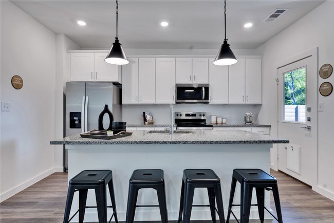 Kitchen featuring stainless steel appliances, visible vents, white cabinets, a sink, and a kitchen breakfast bar | Image 13