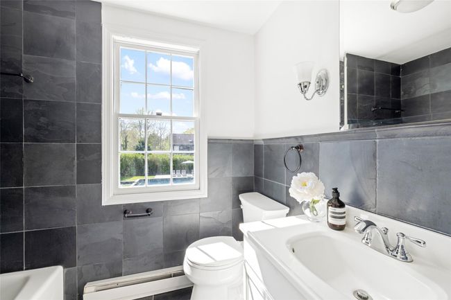 Full bathroom with tile walls, a baseboard radiator, a healthy amount of sunlight, and a sink | Image 16