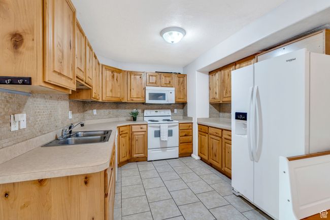 Kitchen featuring white appliances, backsplash, light countertops, and light tile patterned floors | Image 5