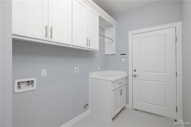 Laundry area featuring hookup for a washing machine, cabinet space, light tile patterned floors, and electric dryer hookup | Image 13