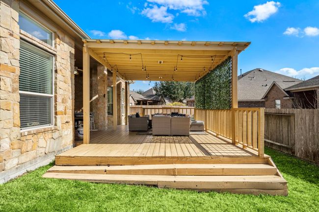 The spacious covered patio, enhanced with a pergola, offers a charming seating area for entertaining or relaxation. The wood decking complements the stone exterior and overlooks the lush green space, creating a seamless blend of indoor comfort and tranquil outdoor living. | Image 36