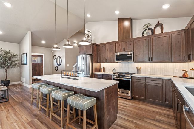 Kitchen with appliances with stainless steel finishes, a center island, vaulted ceiling, decorative backsplash, and wood finished floors | Image 42