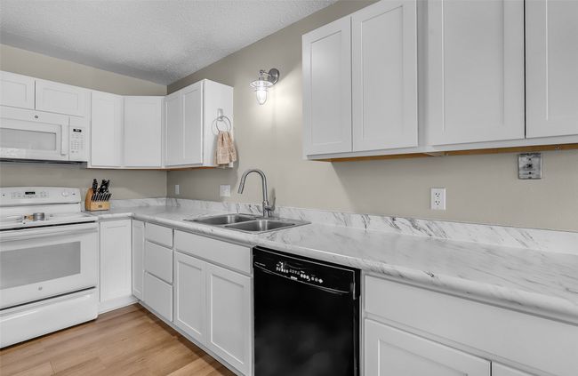 Kitchen with white appliances, a sink, white cabinetry, light wood-style flooring, and a textured ceiling | Image 14