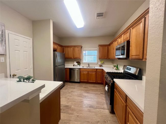 Kitchen with appliances with stainless steel finishes, light wood finished floors, light countertops, and brown cabinetry | Image 12