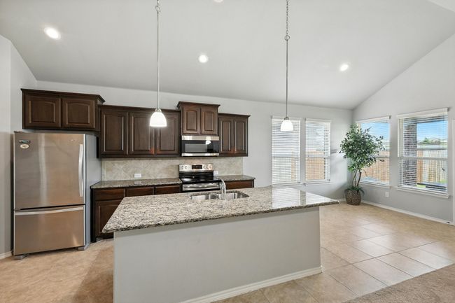 Kitchen featuring appliances with stainless steel finishes, vaulted ceiling, dark brown cabinets, decorative backsplash, and light stone counters | Image 6