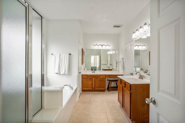 Entering the primary bath, you’re greeted by a spacious layout featuring a separate shower and soaking tub to the left, dual vanities including a dedicated makeup area straight ahead, and private water closet tucked beside. Two doors on the right reveal a generous walk-in closet. | Image 19