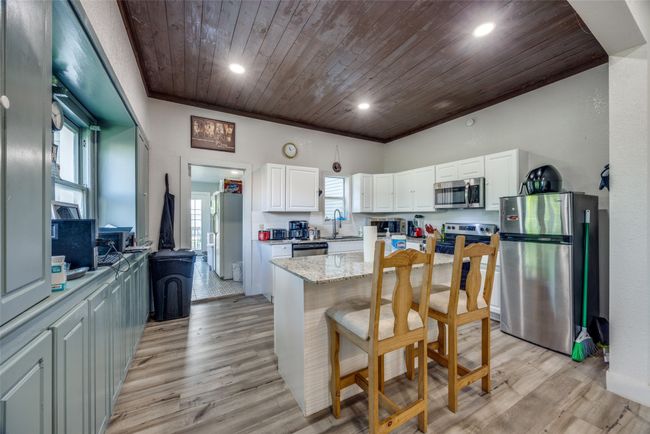 Kitchen featuring stainless steel appliances, wooden ceiling, white cabinets, a breakfast bar, and a sink | Image 4