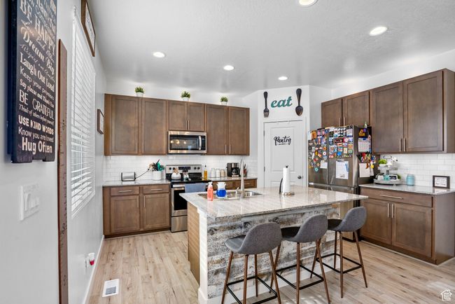 Kitchen with light wood-style flooring, visible vents, a kitchen bar, decorative backsplash, and appliances with stainless steel finishes | Image 8