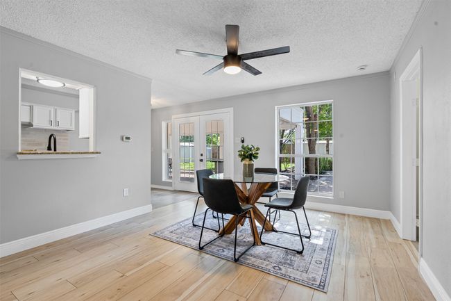 Dining room featuring french doors, light wood-type flooring, a textured ceiling, a ceiling fan, and ornamental molding | Image 10