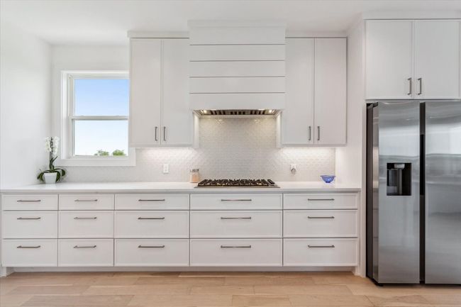 Kitchen with appliances with stainless steel finishes, custom exhaust hood, backsplash, light countertops, and white cabinetry | Image 16