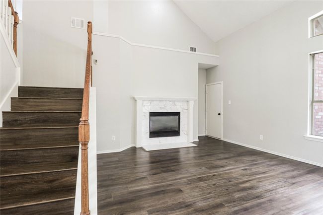 Unfurnished living room with high vaulted ceiling, dark wood-type flooring, stairs, a high end fireplace, and baseboards | Image 5