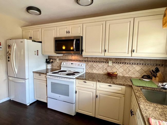 Kitchen featuring white appliances, backsplash, a sink, white cabinetry, and dark wood-type flooring | Image 5